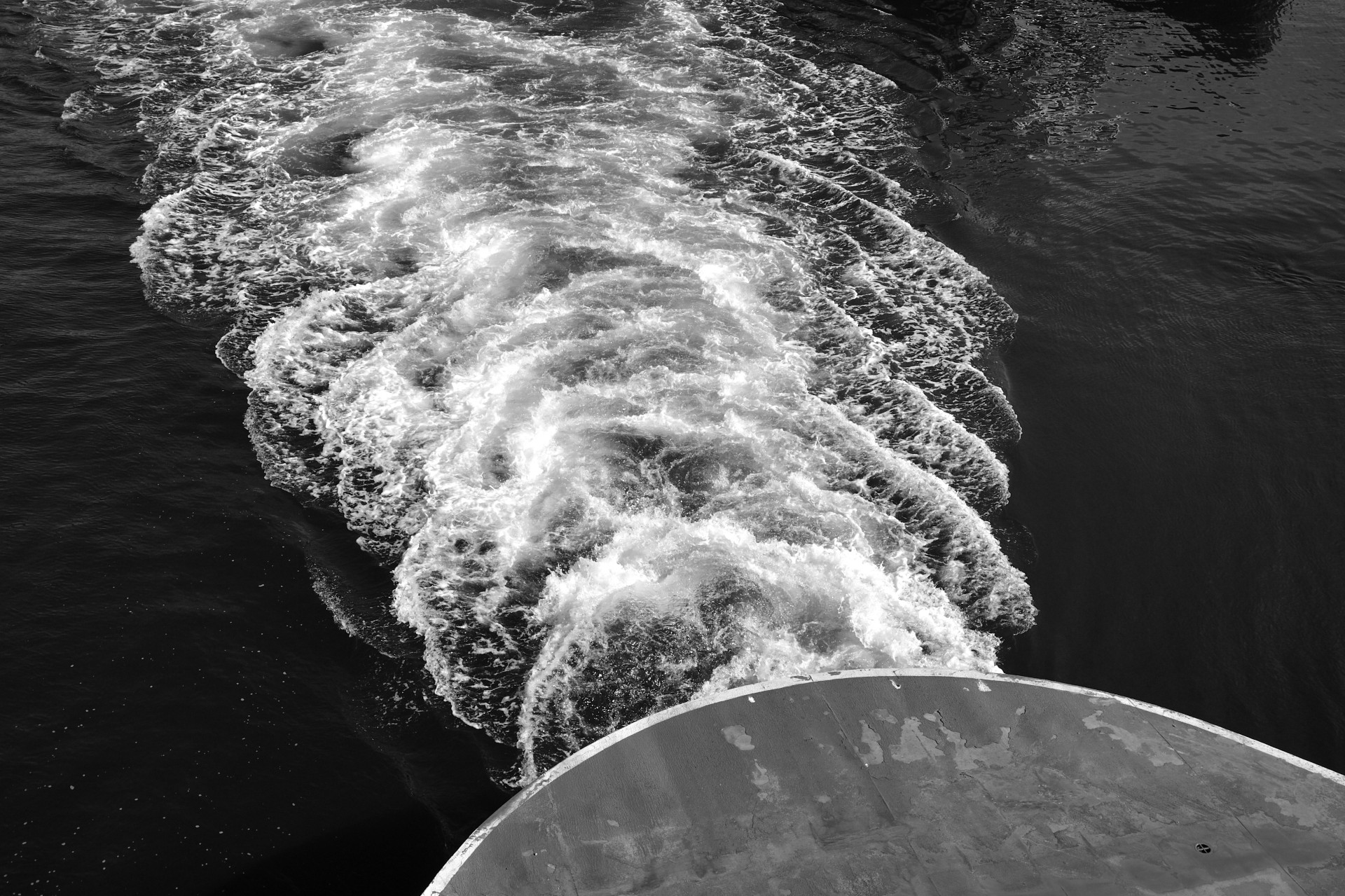 Churning white wake trailing behind the stern of a ship on dark water